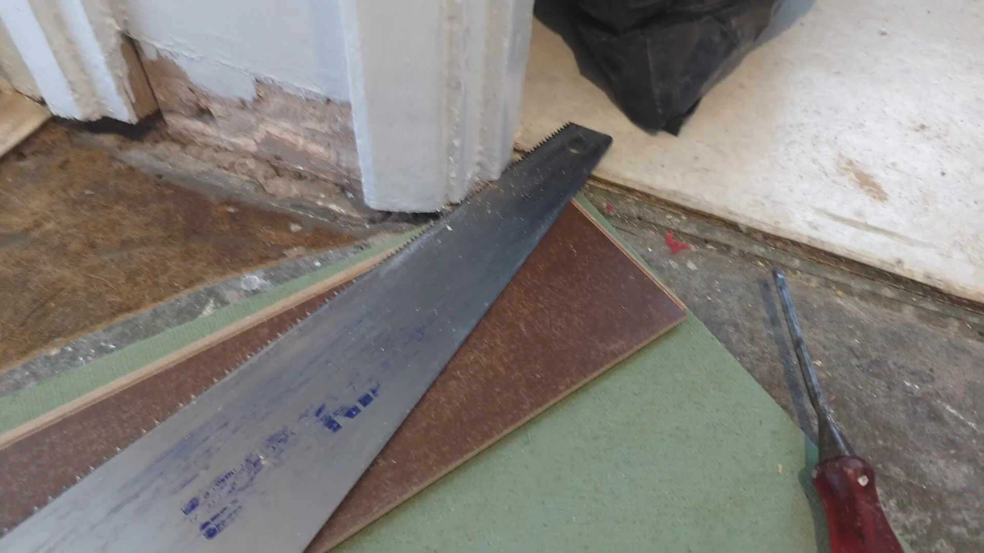 Handsaw cutting under a door lining, running flat on an offcut of laminate laid on the fibreboard underlay