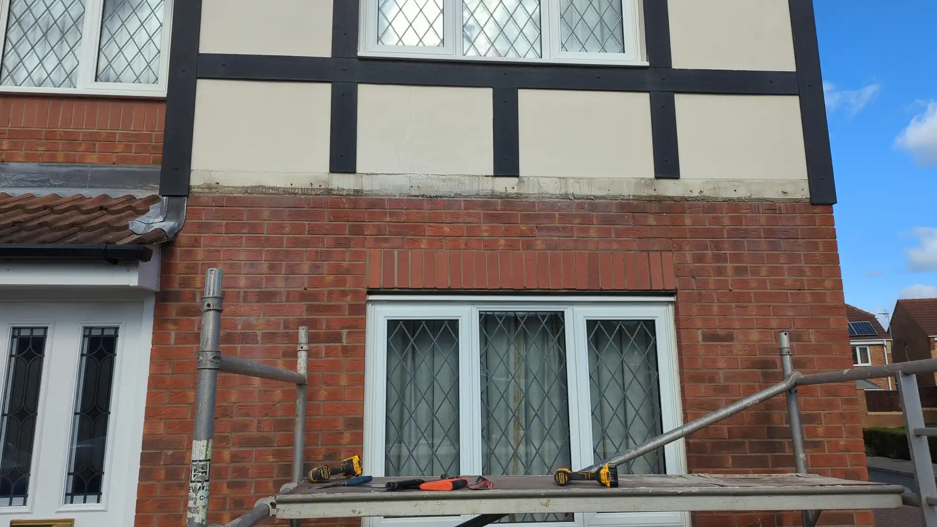 Failed mock-Tudor board removed from the render-to-brick junction, with scaffold tower access