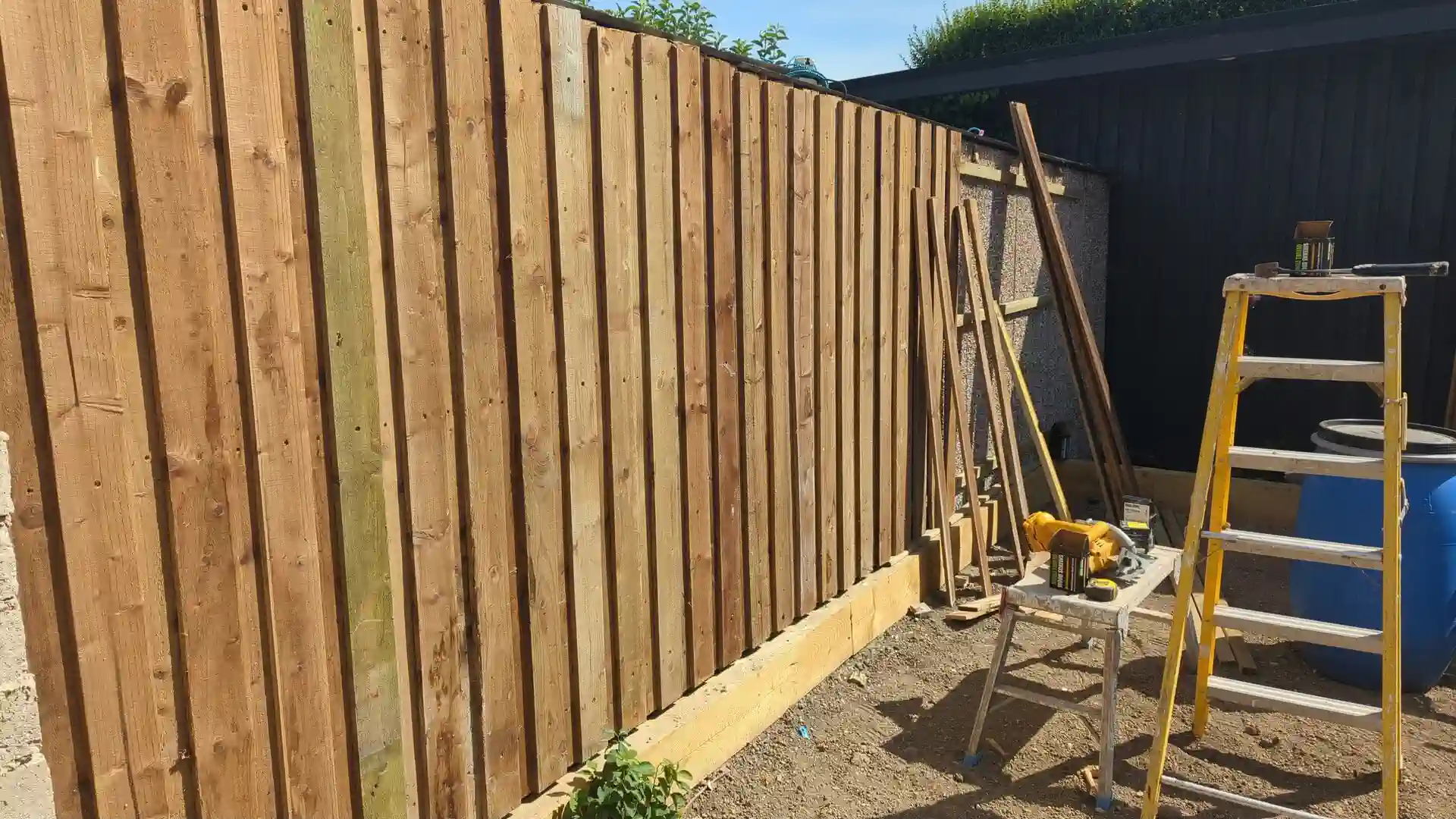 Vertical rough-sawn treated timber boards being screwed to the battens
