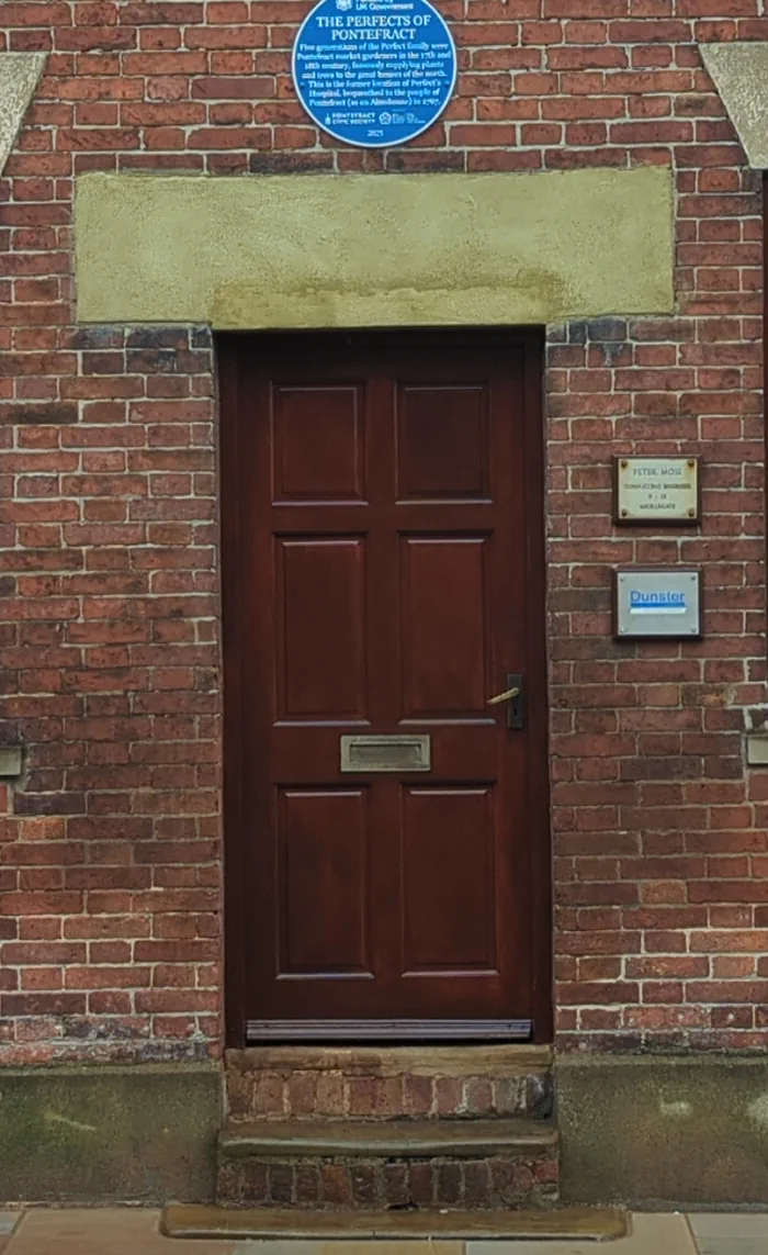 Refurbished timber entrance door at 18-22 Micklegate, Pontefract, finished in mahogany woodstain beneath the Perfects of Pontefract blue plaque
