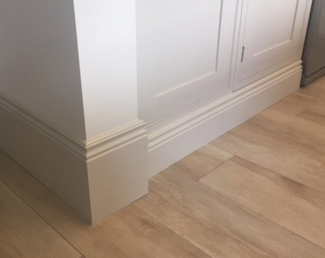 Tall moulded skirting board fitted around an internal corner beside fitted wardrobes
