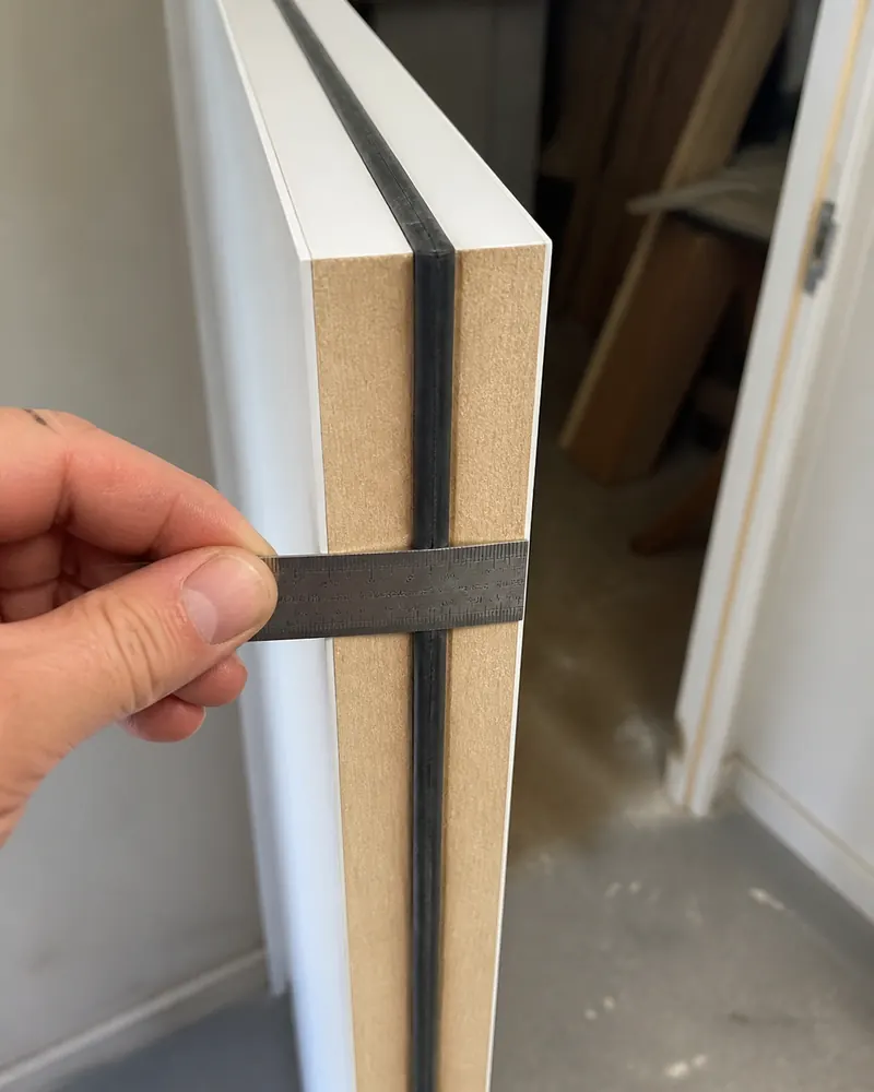 Steel rule held against the edge of a fire door, showing its thickness and the intumescent seal in the groove