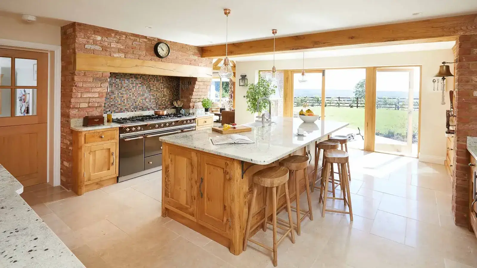 Bespoke timber kitchen with an island, oak beams and exposed brick, opening onto countryside